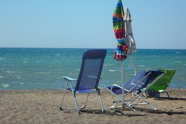 Zwei blaue Stühle und eine grüne Sonnenliege mit zwei zusammengefalteten Sonnenschirmen stehen am Strand Zwei blaue Stühle und eine grüne Sonnenliege mit zwei zusammengefalteten Sonnenschirmen stehen am Strand