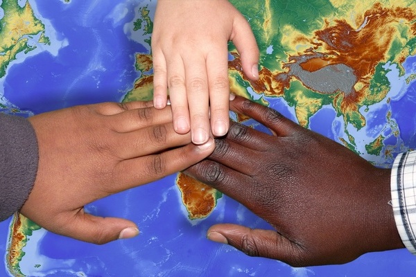 3 Hände mit unterschiedlicher Hautfarbe berühren sich- im Hintergrund eine zeichnerische Darstellung der Kontinente