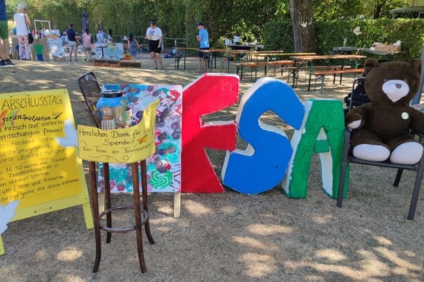 Plakat Abschluss Ferienspielaktion, Spendenkssle, aufgestellte Buchstaben FSA und Teddybr auf einem Stuhl