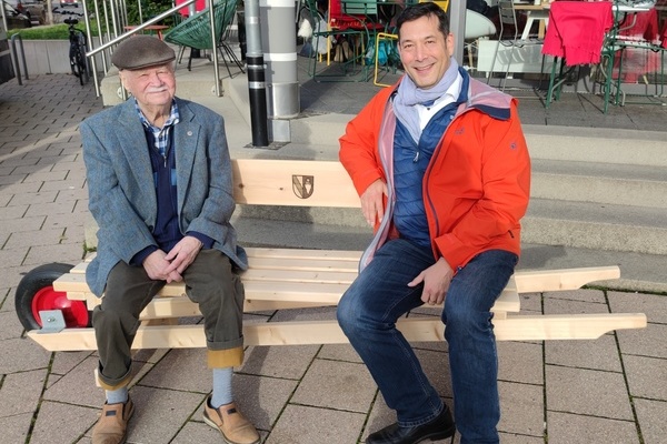 v.l.n.r.: Ein Bürger sitzt zusammen mit Bürgermeister Markus Hollemann auf dem mobilen Schwätzbänkle