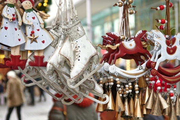 Rot-weiße Engel- und Schlittschuhfiguren sowie Schaukelpferde mit Glöckchen aufgehängt an einem Weihnachtsmarktstand