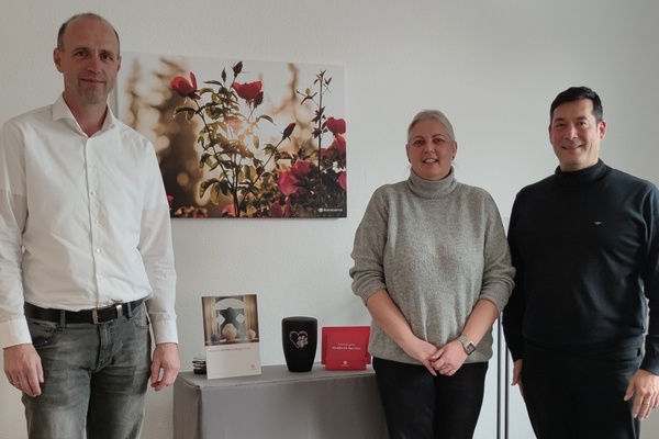 Herr Thorsten Hermes (Abteilungsleiter Filialmanagement), Frau Sandra Gall (Gebietsleiterin Baden-Württemberg), Bürgermeister Markus Hollemann stehend vor einem Rosen-Bild und einer Urne in der Mitte Herr Thorsten Hermes (Abteilungsleiter Filialmanagement), Frau Sandra Gall (Gebietsleiterin Baden-Württemberg), Bürgermeister Markus Hollemann stehend vor einem Rosen-Bild und einer Urne in der Mitte