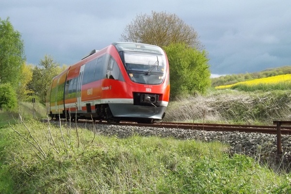 Roter Nahverkehrszug der Deutschen Bahn f&auml;hrt durch gr&uuml;ne Landschaft