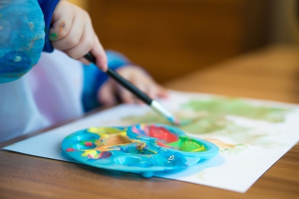 Tisch, Papier, Pinsel, Farbpalette, die Hand eine malenden Kindes