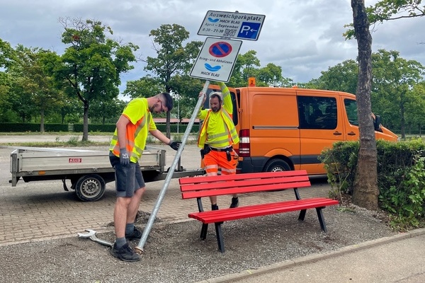 Stefan Schill (links) und Matthias Nbling vom Bauhof errichten die Beschilderung der neuen Bring- und Abholzone am MACH BLAU - mit Bnkle fr Wartende. Foto: Katharina Schrader, Gemeinde Denzlingen