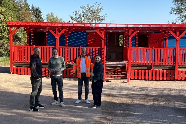Rotblaue Kindergartenhütte, davor vier Personen Rotblaue Kindergartenhütte, davor vier Personen