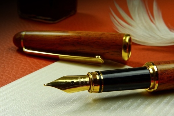 goldener Füllfederhalter auf weißem Papier, im Hintergrund eine weiße Feder goldener Füllfederhalter auf weißem Papier, im Hintergrund eine weiße Feder