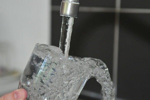 Aus dem Wasserhahn flie&szlig;t Wasser in ein Glas
