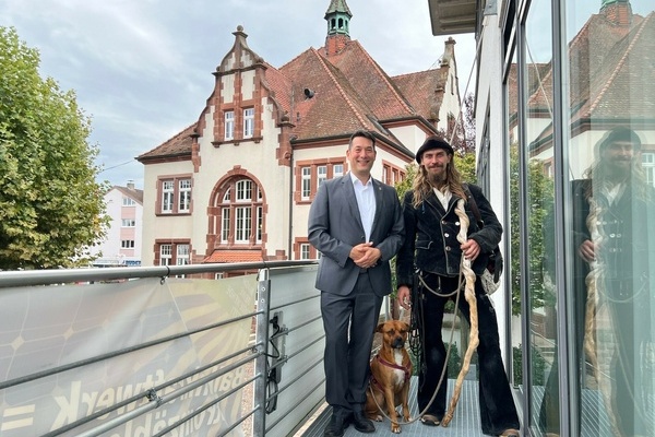 Wandergeselle Tom Adler mit seinem Hund Lotus (rechts) und B&uuml;rgermeister Markus Hollemann auf dem Balkon am Rathausplatz. Foto: Gemeinde Denzlingen