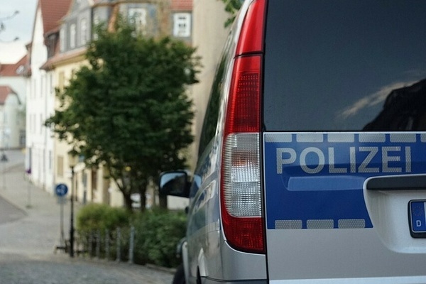 Auf dem Bildausschnitt ist die Rückseite eines Polizeiautos und der Schriftzug Polizei in Grau auf blauem Untergrund. In der Ferne sieht man verschwommen eine Straße und einen Baum sowie eine Häuserreihe. Auf dem Bildausschnitt ist die Rückseite eines Polizeiautos und der Schriftzug Polizei in Grau auf blauem Untergrund. In der Ferne sieht man verschwommen eine Straße und einen Baum sowie eine Häuserreihe.