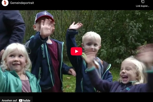 Szene aus dem neuen Denzlinger Gemeindeportrait: winkende Kinder, im Hintergrund grne Strucher