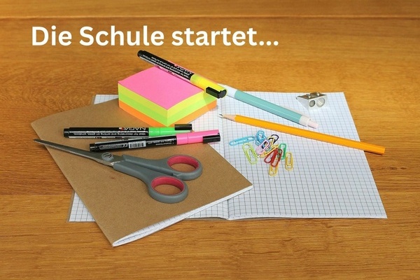 Die Schule startet ... Schulutensilien auf einem Tisch, weiße Schrift auf hölzernem Untergrund Die Schule startet ... Schulutensilien auf einem Tisch, weiße Schrift auf hölzernem Untergrund