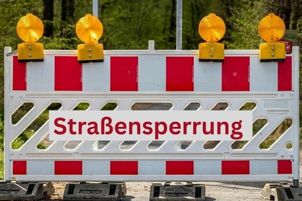 Straensperrung - rote Schrift auf weiem Untergrund und Verkehrsabsperrung mit organgenen Warnleuchten